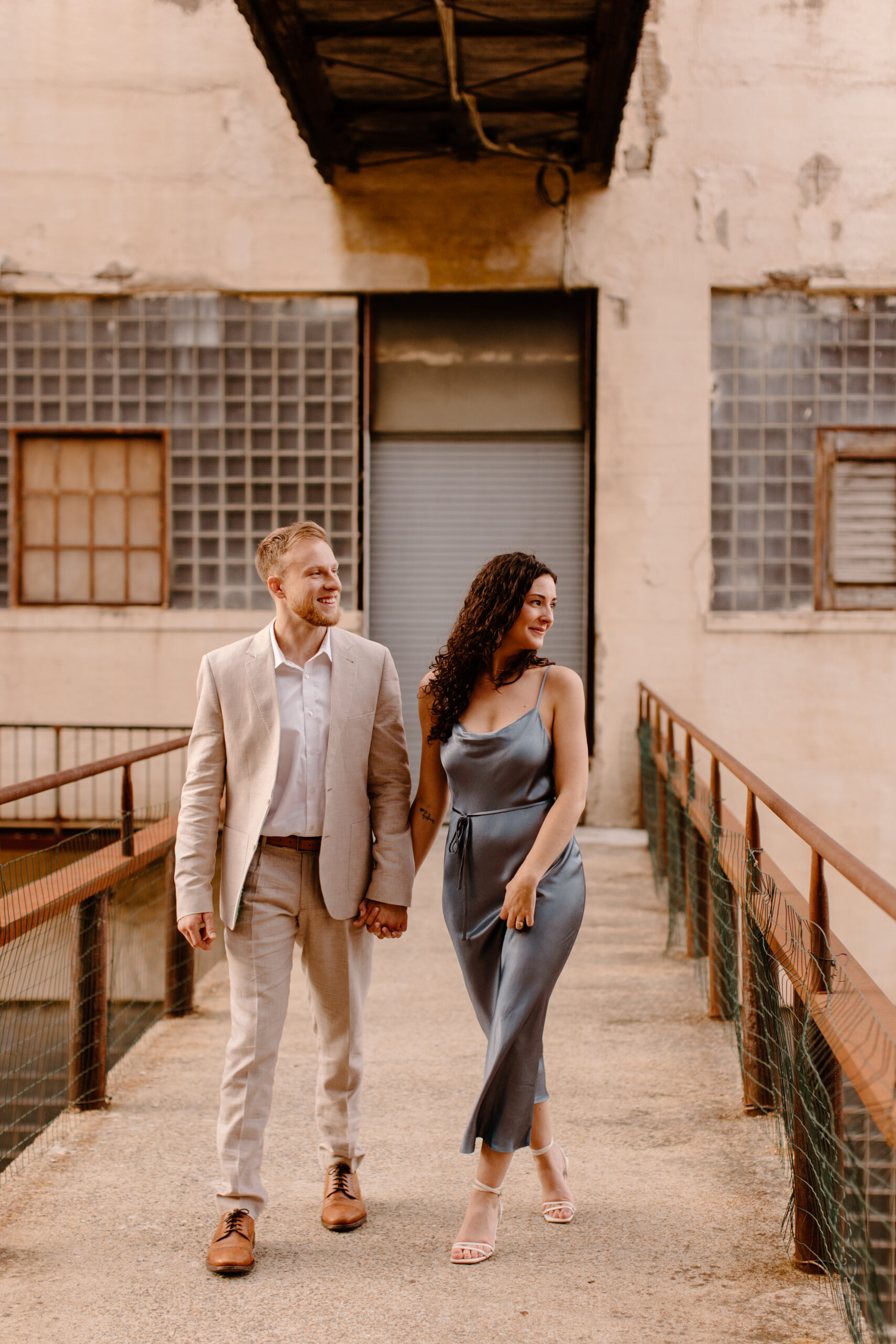 An engaged couple walking through Clipper Mill, Baltimore holding hands.